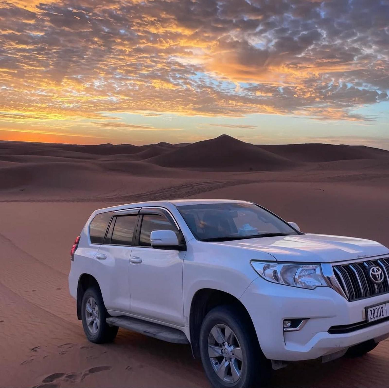 A white 4x4 on the dunes at Erg Chebbi under a sunrise sky