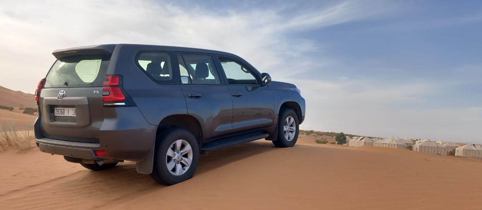 Our 4x4 parked on the red sand at Erg Chebbi, with the tents of a desert camp behind